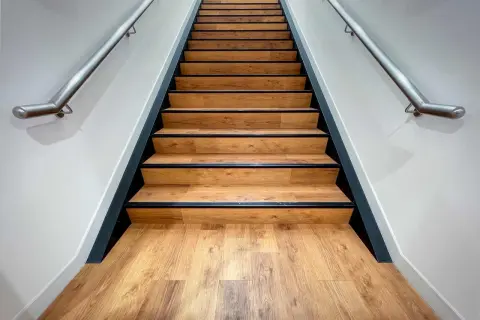 Moderne Treppe mit Holzoptik-Belag. Die Betonstufen sind professionell verkleidet, mit schwarzer Kante und Edelstahl-Handlauf.