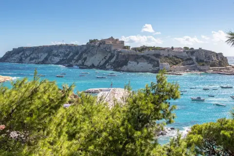 Vista panoramica del paese delle Isole Tremiti, con case bianche arroccate su scogliere a picco sul mare turchese, punteggiato da barche.