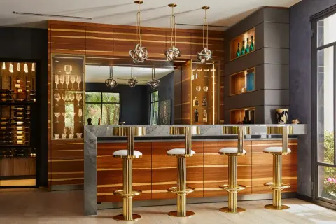 Luxurious home bar ideas featuring a marble countertop, wood cabinetry, gold bar stools, and a wine display.