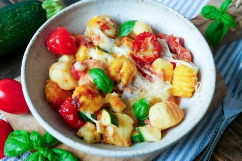 Herzhaftes Gnocchi Auflauf Rezept mit Tomaten, Zucchini und geschmolzenem Käse, garniert mit frischem Basilikum.
