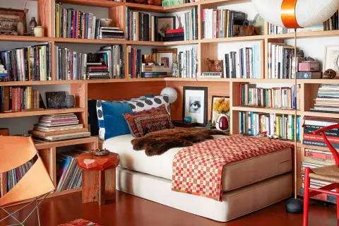 Gemütliches Lesezimmer einrichten mit Bücherregalen voller Bücher, einem Bett, einem Ledersessel und einem roten Stuhl.