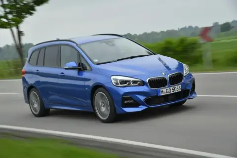 Niebieskie BMW 220i na drodze, z zielonymi polami po bokach.