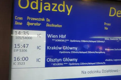 Tablica odjazdów pociągów pokazuje, jak sprawdzić opóźnienie pociągu. Widać opóźnione pociągi do Wiednia, Krakowa i Olsztyna.
