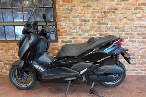 Czarny skuter Yamaha X-Max 125 na tle ceglanej ściany i okna.