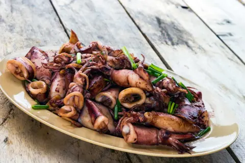 Assiette d'encornets sautés, une délicieuse recette encornet, garnie de ciboule fraîche sur une table en bois.