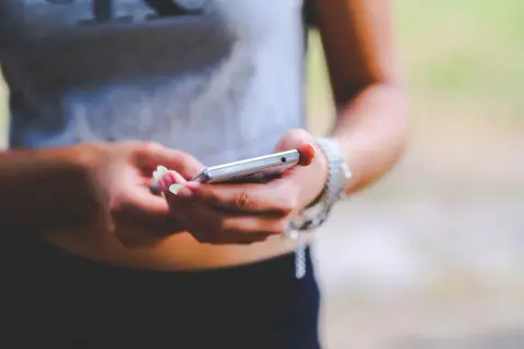 Dłonie z zadbanymi paznokciami trzymają srebrny telefon. To zrzut ekranu Samsunga, uchwycony w letnim otoczeniu.