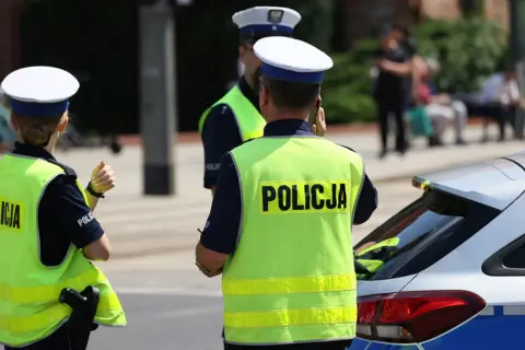 Policjanci w kamizelkach odblaskowych stoją obok radiowozu. Czy policja może wejść na teren prywatny bez nakazu?