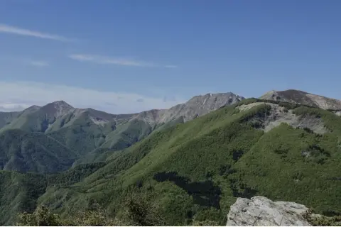 Panoramica dei colli bolognesi in moto, con montagne verdi sotto un cielo azzurro.