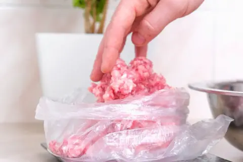 Dłoń wkłada mięso mielone do woreczka na wadze. Tak, mięso mielone można mrozić, by zachować jego świeżość.