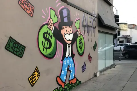 A vibrant graffiti drawing of the Monopoly Man, clutching bags of money, stands proudly on a wall. Dollar bills rain down around him, a testament to his wealth.