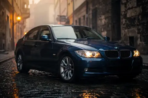 Ciemnoniebieskie BMW E90 2.0 benzyna na mokrej, brukowanej uliczce w starym mieście.