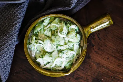 Salade de concombre à la crème, garnie d'aneth frais, servie dans un bol en céramique jaune sur une table en bois rustique.