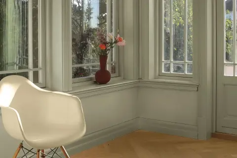 En ljus hall med en vit stol och en vas med blommor på fönsterbrädan. Väggarna är målade i en lugn grön nyans, vilket ger en harmonisk känsla.