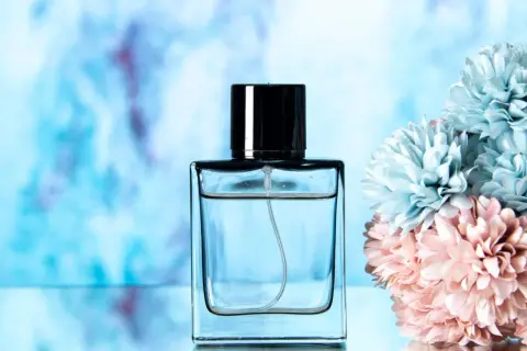 Elegancka butelka perfum lataffa z czarną nakrętką, obok pastelowych kwiatów.