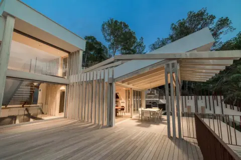 Terraza moderna con suelo de madera Accoya, pérgola y fachada acristalada.