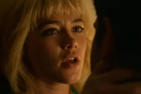 Zbliżenie na Florence Pugh w jednym z jej filmów. Jej blond włosy i wyraziste oczy przyciągają uwagę.
