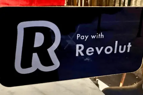 Znak informuje, jak płacić Revolutem. Widoczny duży symbol "R" i napis "Pay with Revolut".