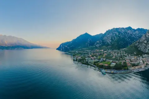 Panoramica del Lago di Garda con montagne imponenti e una città pittoresca. Perfetto per scoprire le **Unternehmungen Gardasee**.