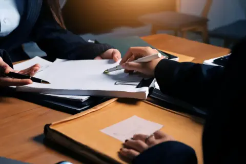 Dwie osoby przy biurku omawiają dokumenty. Zastanawiasz się, ile kosztuje prawnik?