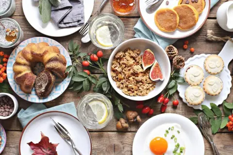 Leckere Brunch-Ideen: Marmorkuchen, Pancakes, Müsli, Obst und kleine Törtchen auf rustikalem Holztisch.