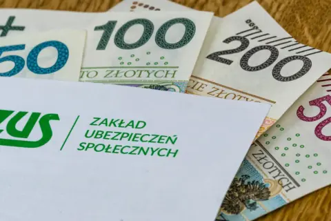 Koperta ZUS z logo i napisem "Zakład Ubezpieczeń Społecznych" na tle polskich banknotów 50, 100, 200 i 500 zł. Symbolizuje świadczenie kompensacyjne.