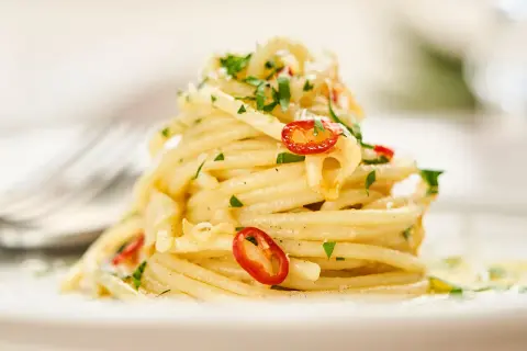 Ein Teller Spaghetti Aglio e Olio, garniert mit Petersilie und Chilischeiben. Ein Klassiker der besten italienischen Pasta Rezepte.