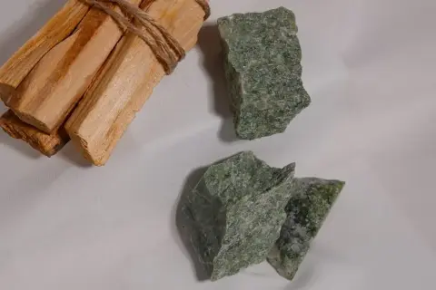 Surowe kawałki jadeitu w odcieniach zieleni, obok wiązki drewna Palo Santo.