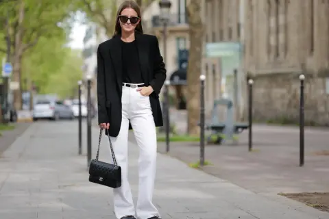 Frau in schicker Business-Kleidung mit schwarzem Blazer, weißer Hose und Chanel-Tasche.