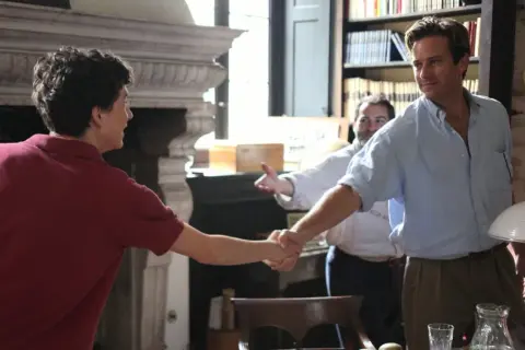 Elio und Oliver schütteln sich die Hände, ein Moment, der an "Call Me By Your Name 2" erinnert. Ein Mann im Hintergrund lächelt.
