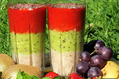 Warstwowy koktajl owocowy z truskawkami, kiwi i bananem, ozdobiony startą czekoladą. Obok owoce: winogrona, kiwi, truskawki, banan.