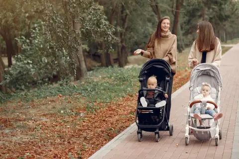 Dwie kobiety spacerują z dziećmi w wózkach po parku jesienią.