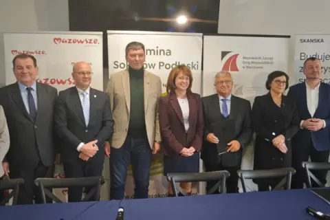 Grupa osób pozuje do zdjęcia na tle banerów informujących o budowie obwodnicy Sokołowa Podlaskiego.
