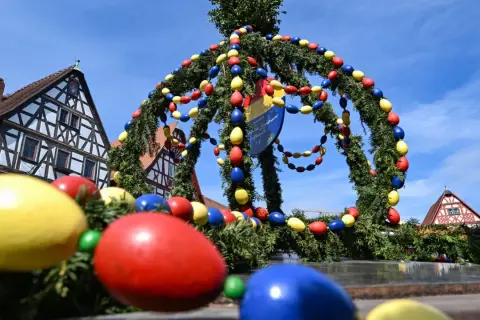 Bunte Ostereier schmücken einen Tannenkranz vor Fachwerkhäusern. Es gibt Karsamstag, die Vorfreude auf Ostern ist spürbar.