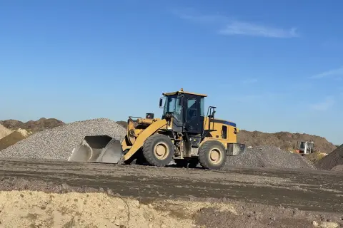 Chargeuse jaune en action pour décaissement de terrain, entourée de tas de gravats et de terre sous un ciel bleu clair.