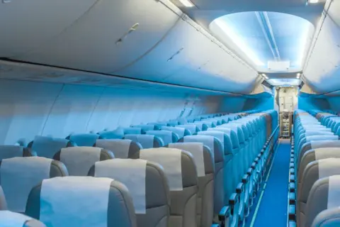 Wnętrze samolotu Boeing 787 LOT. Widok na rzędy pustych siedzeń, które tworzą rozkład miejsc w kabinie pasażerskiej.