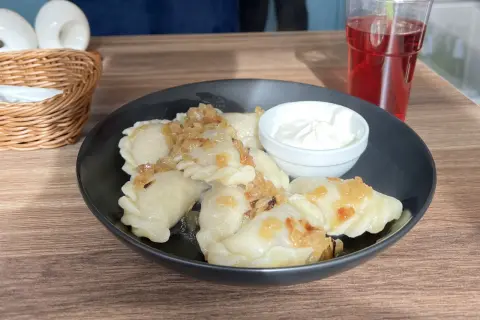 Leckeres Essen in Breslau: Dampfende Pierogi mit Zwiebeln und Sauerrahm, dazu ein rotes Getränk.