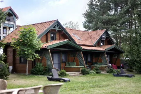 Drewniany domek spa na Mazurach, otoczony zielenią. Leżaki zapraszają do relaksu.