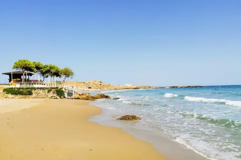 Piękne zakynthos plaże z piaszczystym brzegiem, turkusową wodą i kamienistymi wysepkami. W oddali widać biały domek i zielone drzewa.