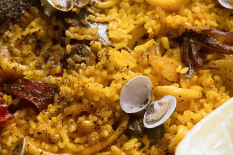 Deliciosa paella en Zaragoza, con arroz amarillo, mejillones, calamares y un toque de limón.
