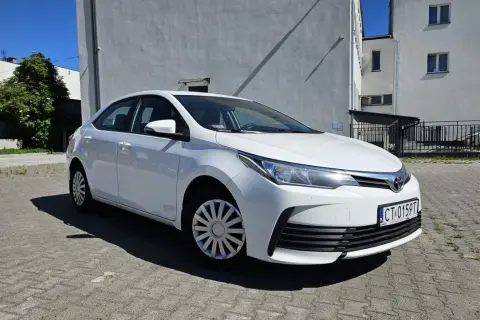 Biała Toyota Corolla 2017 zaparkowana na placu przed budynkiem.