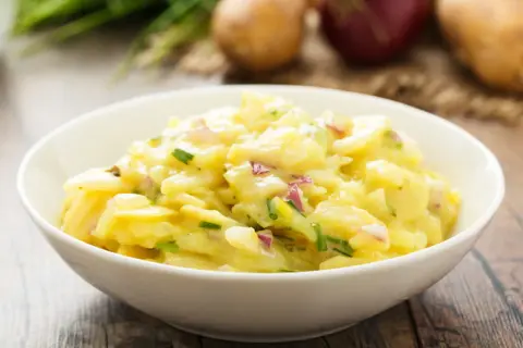 Omas Kartoffelsalat in einer Schüssel, mit Zwiebeln und Schnittlauch, auf einem Holztisch.