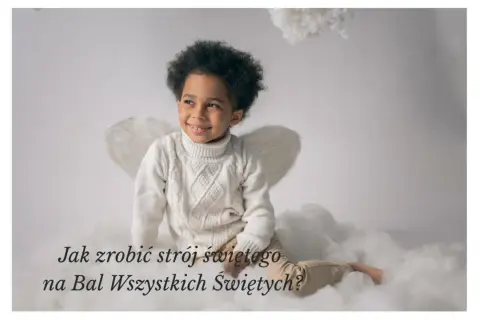 Uśmiechnięty chłopiec w białym swetrze i ze skrzydłami anioła, siedzi na chmurkach. Idealny pomysł na stroje świętych dla dzieci na bal.