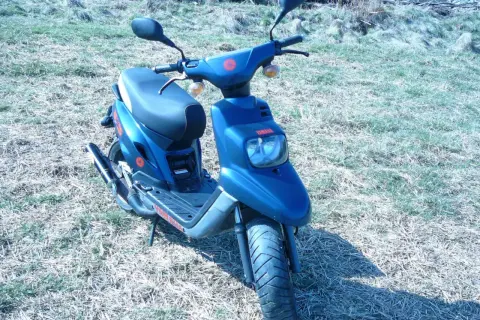 Niebieski skuter Yamaha MBK z czerwonymi akcentami stoi na trawiastym podwórku.
