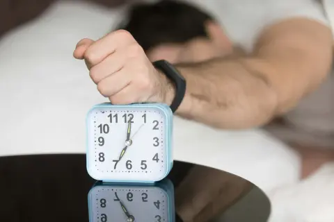 A hand rests on an alarm clock showing 7:00, reflecting the question: is four hours of sleep enough?