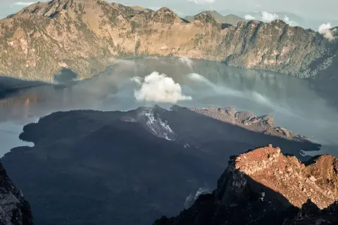 Aktywny wulkan w Indonezji, z dymem unoszącym się z krateru i jeziorem w kalderze.