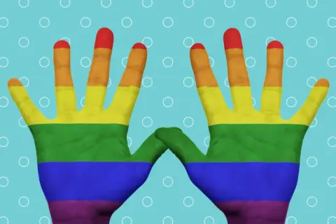 Tęczowe rysunki na ręce, symbolizujące dumę i akceptację, unoszą się na błękitnym tle z białymi kółkami.