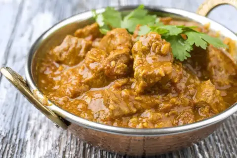 Un savoureux colombo d'agneau, mijoté dans une sauce épicée et garni de coriandre fraîche, servi dans un bol en cuivre.