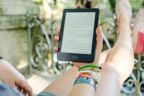 Une personne lit un ebook Kobo dans un jardin, profitant d'un moment de détente avec une collection de 1001 ebooks légal.