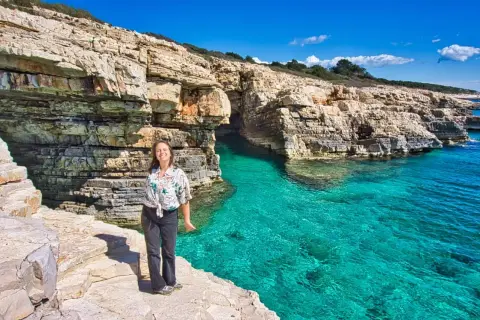 Frau genießt die Sonne an einer felsigen Küste mit türkisfarbenem Wasser. Perfekte pula unternehmungen für einen Urlaub.