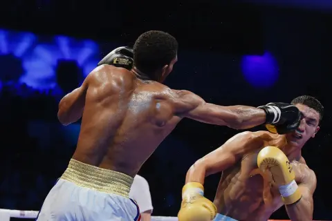 A boxer lands a punch, sweat flying, as the crowd awaits the boxing decisions.